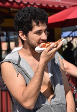 Yakışıklı bir genç adam açık havada bir dilim pizza yeme