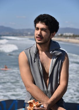 Yakışıklı bir genç mulit-etnik adam okyanusun üzerinde Rıhtımda bir dilim pizza yeme