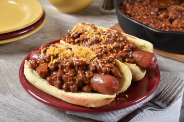 Plump hot dogs topped with chili and grated cheddar cheese clipart