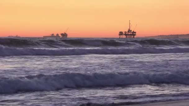 Ondas Batendo Costa Pôr Sol Com Plataformas Perfuração Petróleo Offshore — Vídeo de Stock