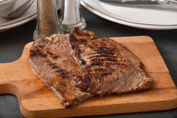 Fresh grilled beef steaks on a cutting board near dinner plates
