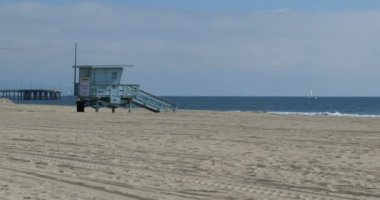 Lifeguard hut on a deserted beach with a pier and sailboat in background