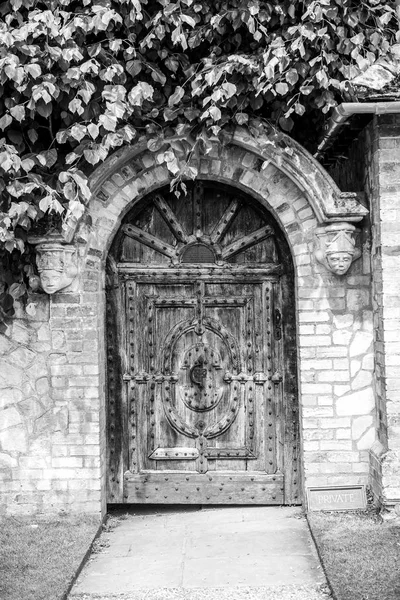 A doorway in a wall, with a canopy of trees, in black and white
