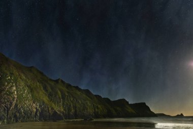 Su kenarında ay ışığı ve gökyüzünde yıldızlar ile geceleri deniz uçurumlar.