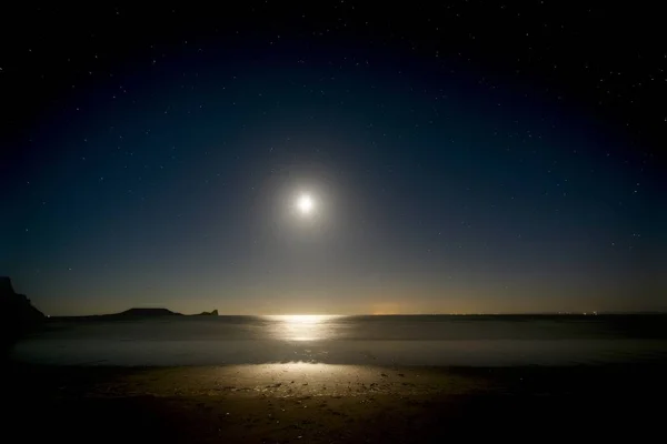 Beach at night with moonlight shining on sea and stars in the sky