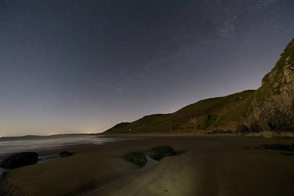 Beach at night with hills in background and stars in the sky