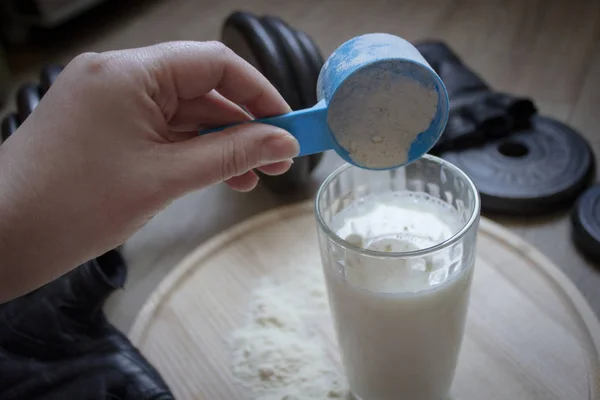 A woman's hand pours the protein powder into a glass of milk.