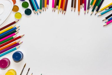 Renkli kalemler, boyalar ve beyaz arka planda fırçalar. Üstten görünüm, kopya alanı.