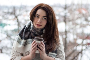Beyaz elbise ve rahat eşarp bir kupa sıcak kakao, çay veya kahve ile tutan güzel bir kadın. Kış veya Noel zaman kavramı.