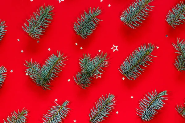 Feliz Natal e Boas Festas cartão de felicitações. Padrão festivo feito de ramos de árvore de Natal azul e estrela de prata em forma de confete em um fundo vermelho. Vista superior, flat lay . — Fotografia de Stock