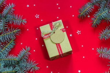 Mutlu Noeller ve Mutlu Tatiller tebrik kartı. Hediye kutusu, mavi Noel ağacı dalları ve kırmızı bir arka plan üzerinde gümüş yıldız şeklinde konfeti. Üstte görüntü.