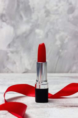 Açık gri arkaplanda kırmızı ruj ve kırmızı kurdele. Moda, makyaj ya da güzellik konsepti. Boşluğu kopyala.