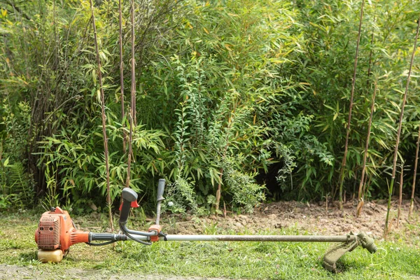 Close up of an old and dirty brush cutter on green grass in the garden.