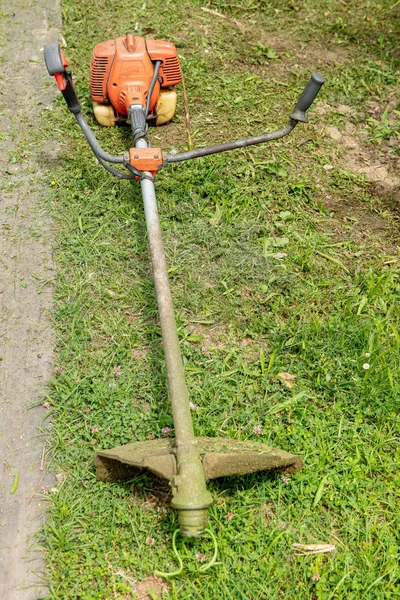 Close up of an old and dirty brush cutter on green grass in the garden.