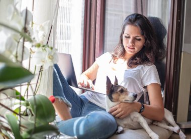 Sevimli dostu genç kadın onun yanında küçük köpek zevk pencere kenarına ev bakimi rahatlatıcı
