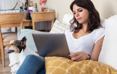 Çekici genç kadın küçük Jack Russell onun yanına bir oturma odası yalan bir dizüstü bilgisayar ile bir kanepede rahatlatıcı