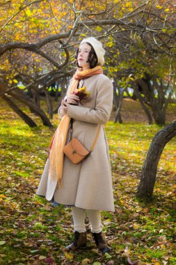 melankolik kadınlar Açık bir palto ve düşen yapraklar elleri ile parkta bir sonbahar gününde bere.