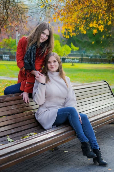 Две Красивые Девушки Солнечный Осенний День Сидят Бок Бок Скамейке — стоковое фото
