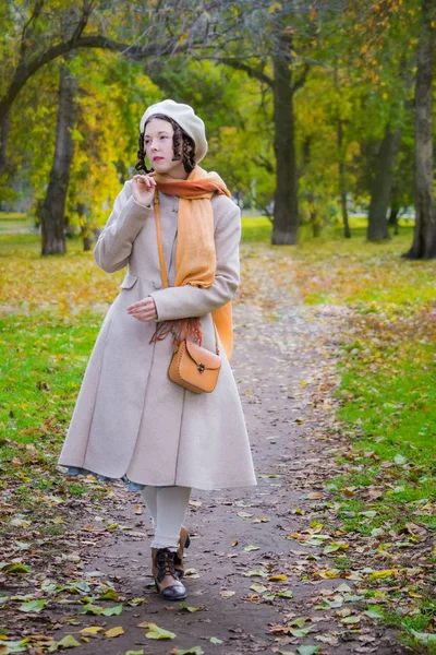 薄手のコートや秋秋葉の間に公園の中を歩く日にベレー帽の女の子が落ち葉を見てください — ストック写真
