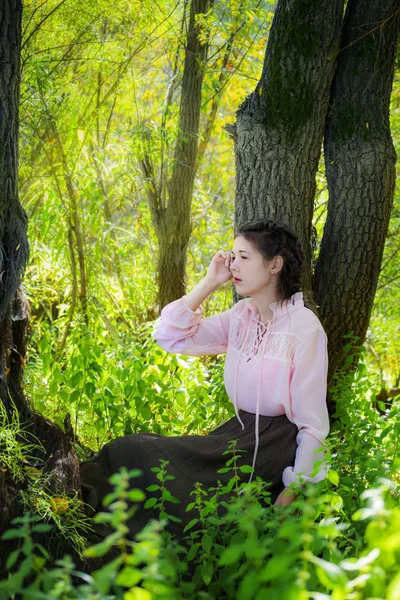 年轻的女孩穿着博霍风格 坐在附近的一棵树在一个神话般的夏季森林 — 图库照片