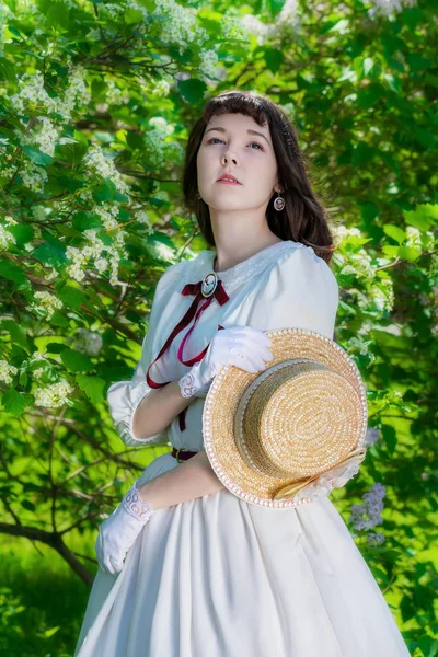 Meisje in een witte jurk en de stro hoed in de buurt van bloemen meidoorn — Stockfoto