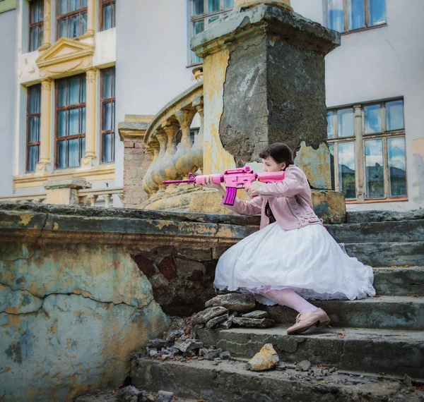 Ragazza in un abito bianco con un fucile rosa gioca airsoft — Foto Stock