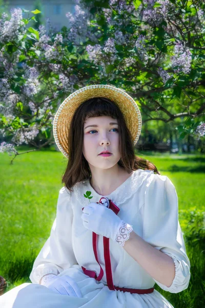 Ragazza con un vestito bianco seduta sotto un albero lilla . — Foto Stock