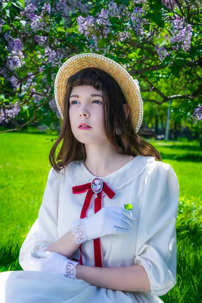 Chica en un vestido blanco sentado debajo de un árbol lilas . — Foto de Stock
