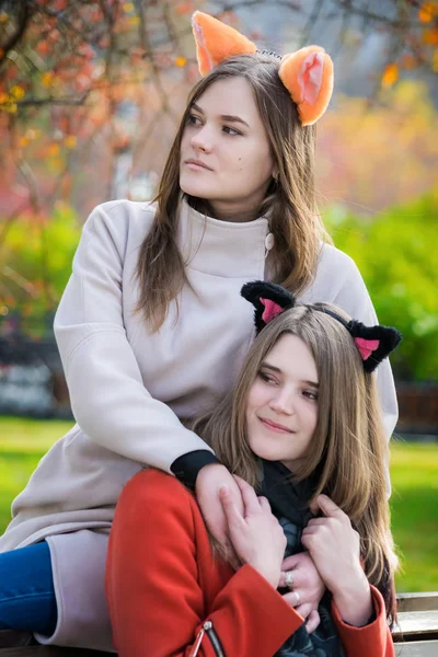 Two beautiful girlfriends sitting side by side on a bench