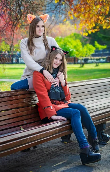Две красивые подруги, сидящие бок о бок на скамейке и сидящие на стуле. — стоковое фото