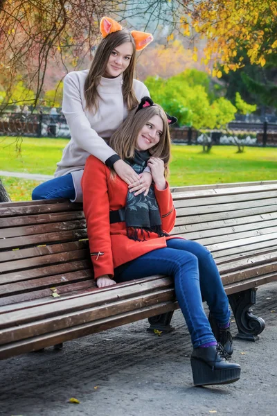 Two beautiful girlfriends sitting side by side on a bench and sm