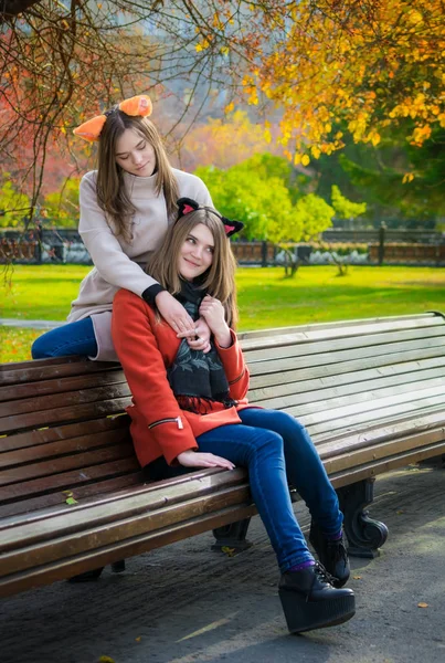 Two beautiful girlfriends sitting side by side on a bench and sm