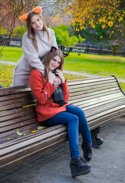Two beautiful girlfriends sitting side by side on a bench and sm