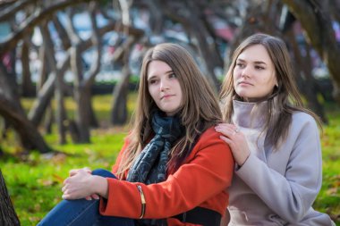 Parkta çimenlerde oturan iki güzel kız arkadaş.