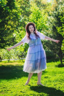 Genç ve güzel bir kız, güneşli bir günde, parkta dans ederek seviniyor..