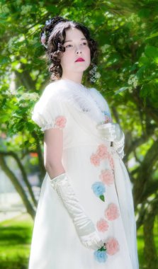 Zarif, uzun, beyaz gelinlikli genç kadın bir bahar bahçesinde çiçek açan ağacın yanında..