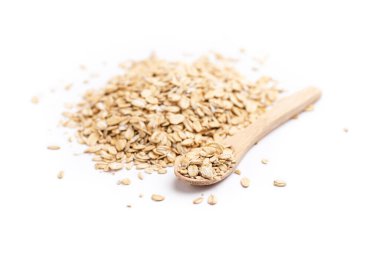 Sağda dolu bir tahta kaşık ve beyaz arka planda izole edilmiş bir yığın yulaf ezmesi.