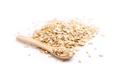 Solda dolu bir tahta kaşık ve beyaz arka planda izole edilmiş bir yığın yulaf ezmesi.