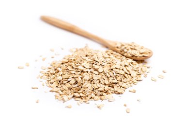 Sağda dolu bir tahta kaşık ve beyaz arka planda izole edilmiş bir yığın yulaf ezmesi.