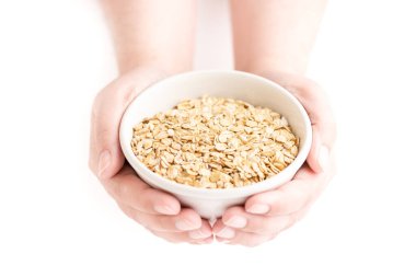 Beyaz bir arka planda bir kadının ellerinin tuttuğu yulaf lapası kasesinin ön görüntüsü.