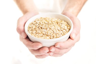 Beyaz arka planda bir adamın ellerinin tuttuğu yulaf lapası kasesinin yakın çekimi.