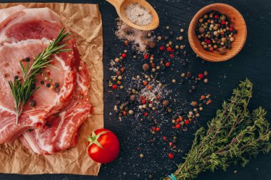 Bir masada baharat, kekik ve biberiye ile pişmemiş çiğ domuz pirzolası