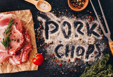 Bir masada baharat ve barbekü çatal ile pişmemiş çiğ domuz pirzolası . Domuz pirzolası yazıt Düz yatıyordu.