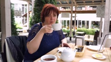 Yetişkin kadın yaz terasında bir kafede aromatik çay içer.