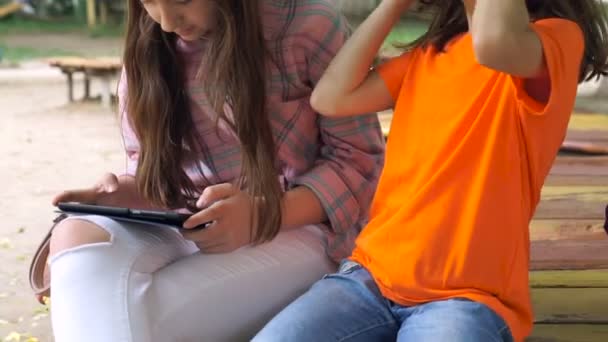 Δύο Κορίτσια Είναι Χρησιμοποιώντας Tablet Εξωτερικούς Χώρους Κάθεται Στο Πάρκο — Αρχείο Βίντεο