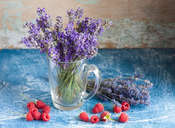 Lavender in vase with raspberry on blue stone background