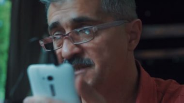 Cep telefonu üzerinde konuşurken gözlüklü bir adam kafede oturmuş.