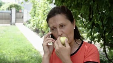 Olgun güzel mutlu kadının bir elma tutan telefonda konuşurken yakın çekim.