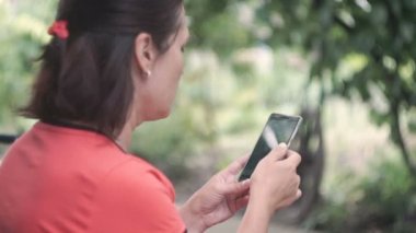 Smartphone dışında yeşil ağaçlar doğa geçmiş vasıl kullanan genç kadın. Genç kadın cep telefonuyla. Kadın mesaj sms telefonunda dışında Park.