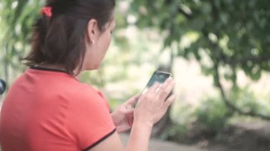 Smartphone dışında yeşil ağaçlar doğa geçmiş vasıl kullanan genç kadın. Genç kadın cep telefonuyla. Kadın mesaj sms telefonunda dışında Park.